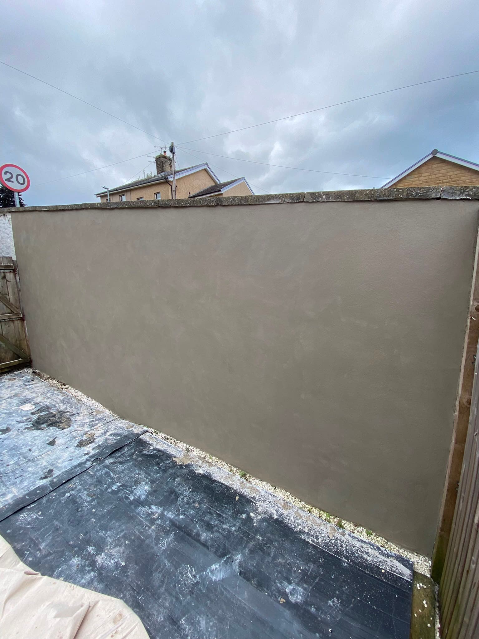 A freshly rendered garden boundary wall finished in a smooth grey render