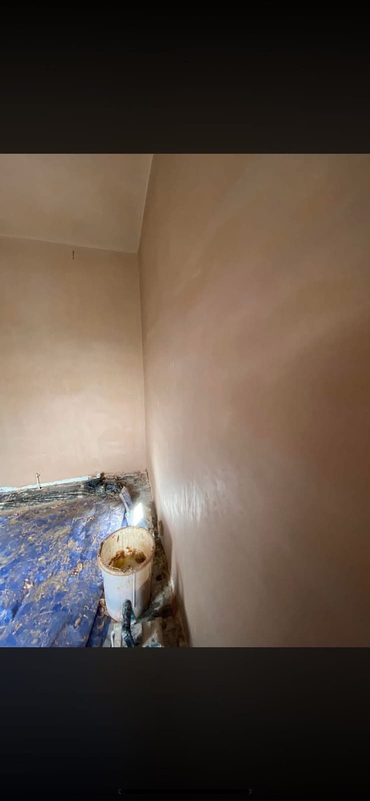 Freshly skimmed walls in the corner of a room, dust sheets and a bucket on the floor