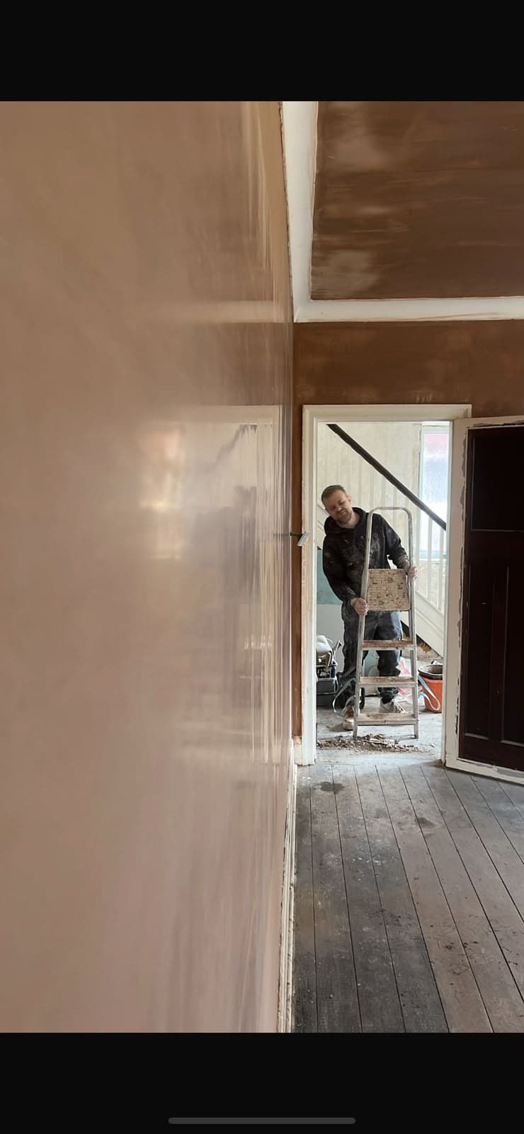 A skimmed hallway wall with a plasterer working near the staircase
