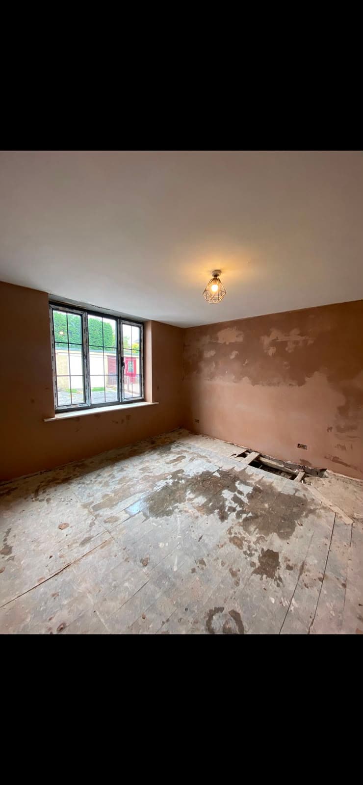 A bedroom mid-plaster with a patched wall and bare floorboards