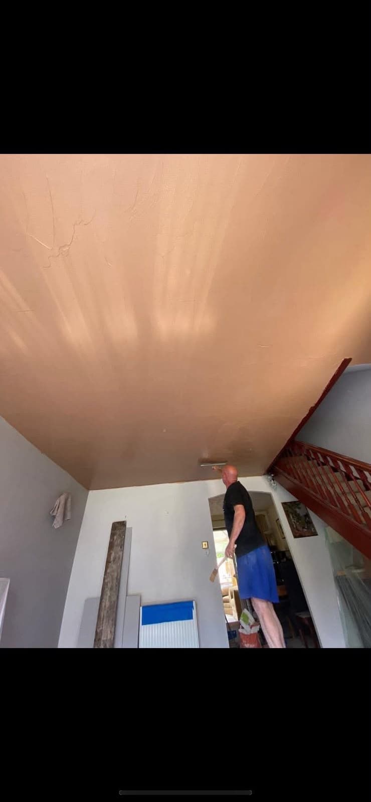 A plasterer applying a mist coat to a stairwell ceiling
