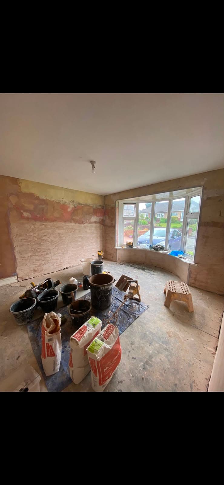 A bay window room mid-plaster with combed adhesive on the wall and bags of Multi Finish