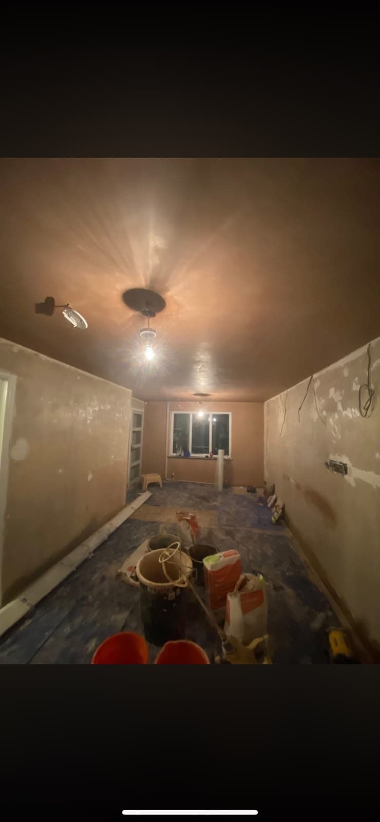 A long skimmed room photographed at night with buckets and plaster bags on the floor