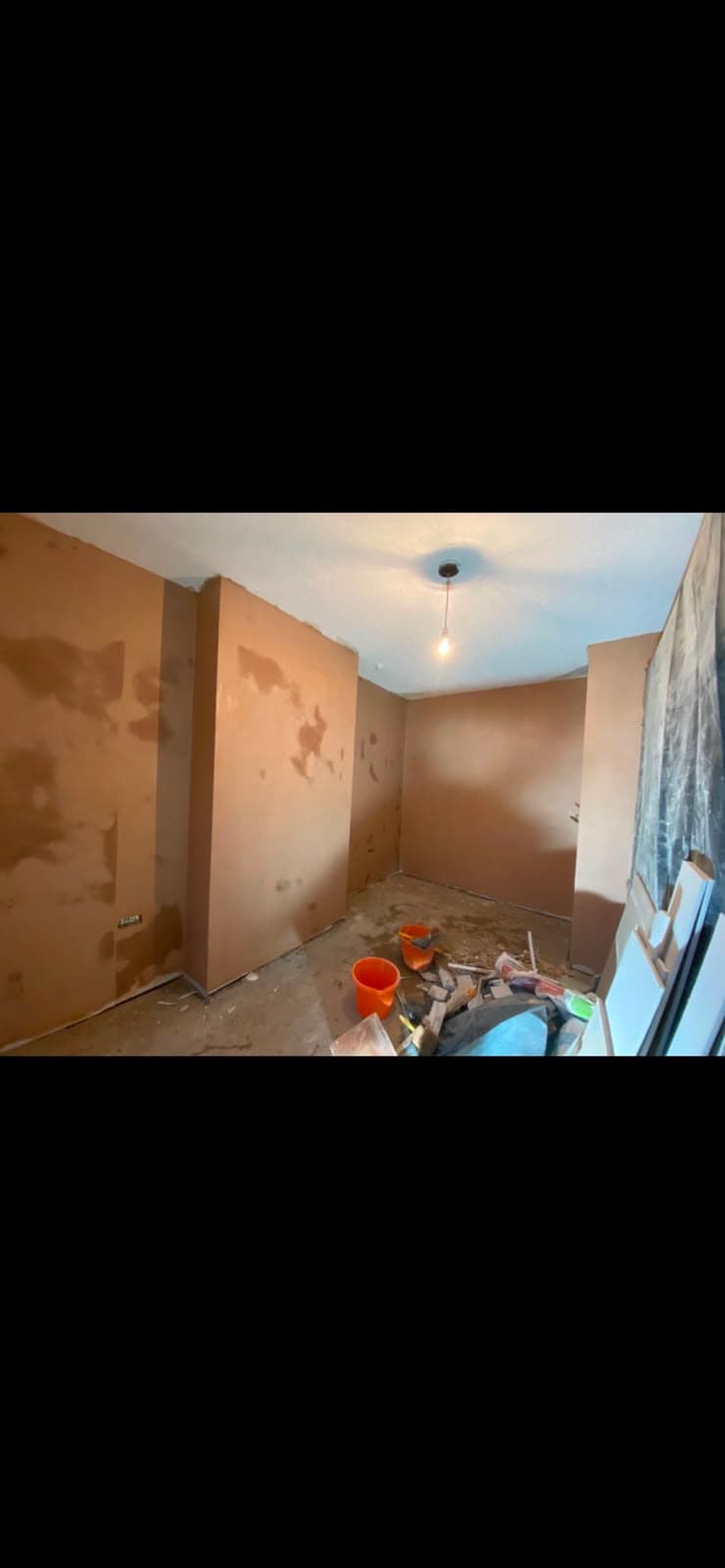 A room mid-skim with patched sections of wall and buckets on the floor