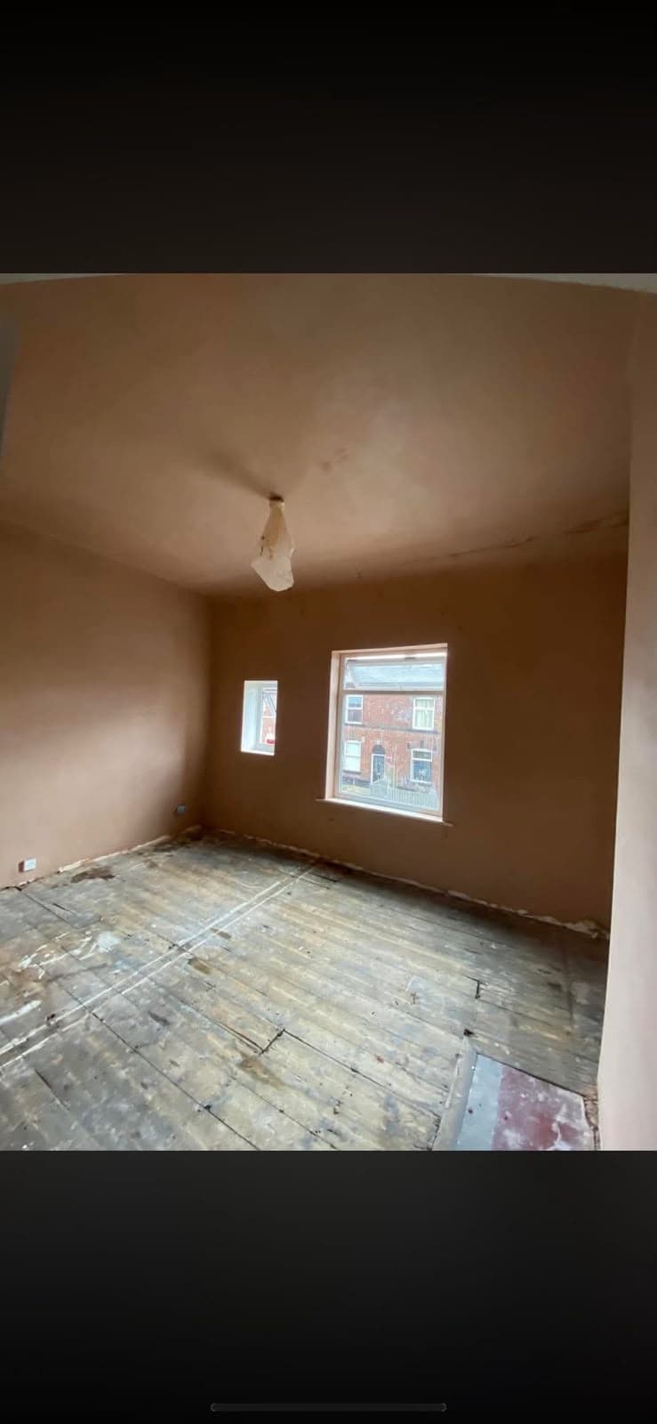 An empty freshly skimmed room with a sash window overlooking the street