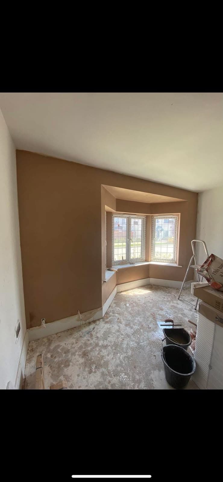 A finished bay window room, freshly skimmed and ready, with a ladder and buckets still out