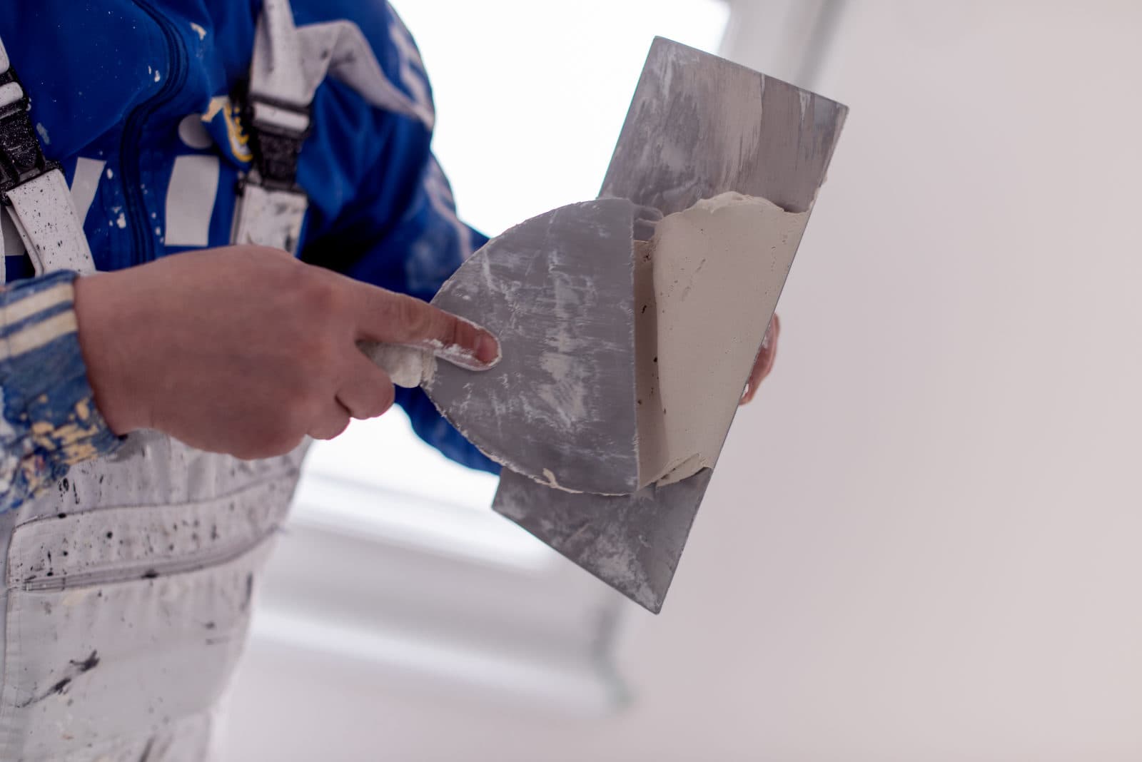 A plasterer working from a ladder and plank to skim a ceiling by lamplight